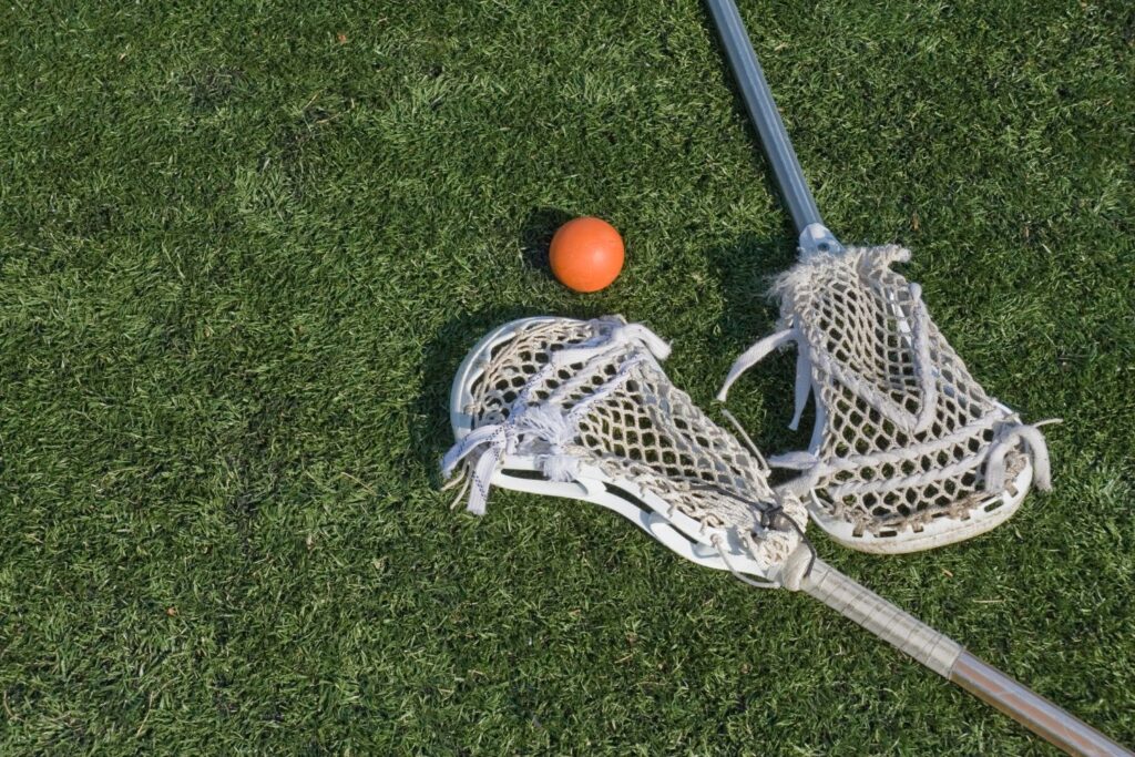 Two lacrosse sticks and a lacrosse ball laying on the ground.